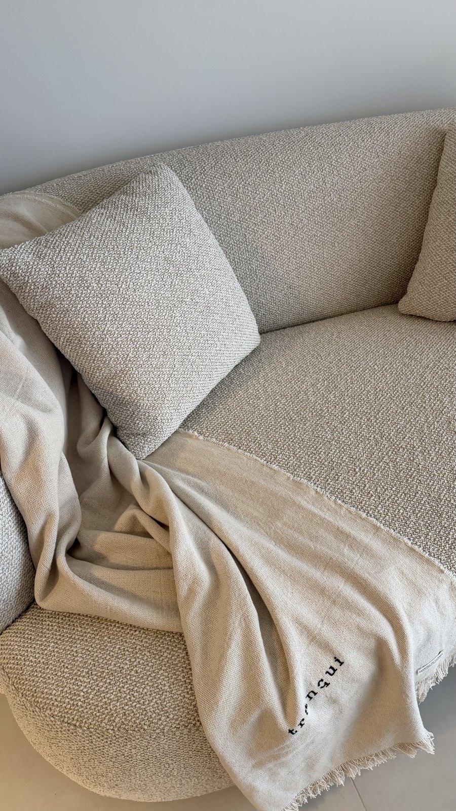 Sillón de bouclé con almohadones y manta de lino con flecos